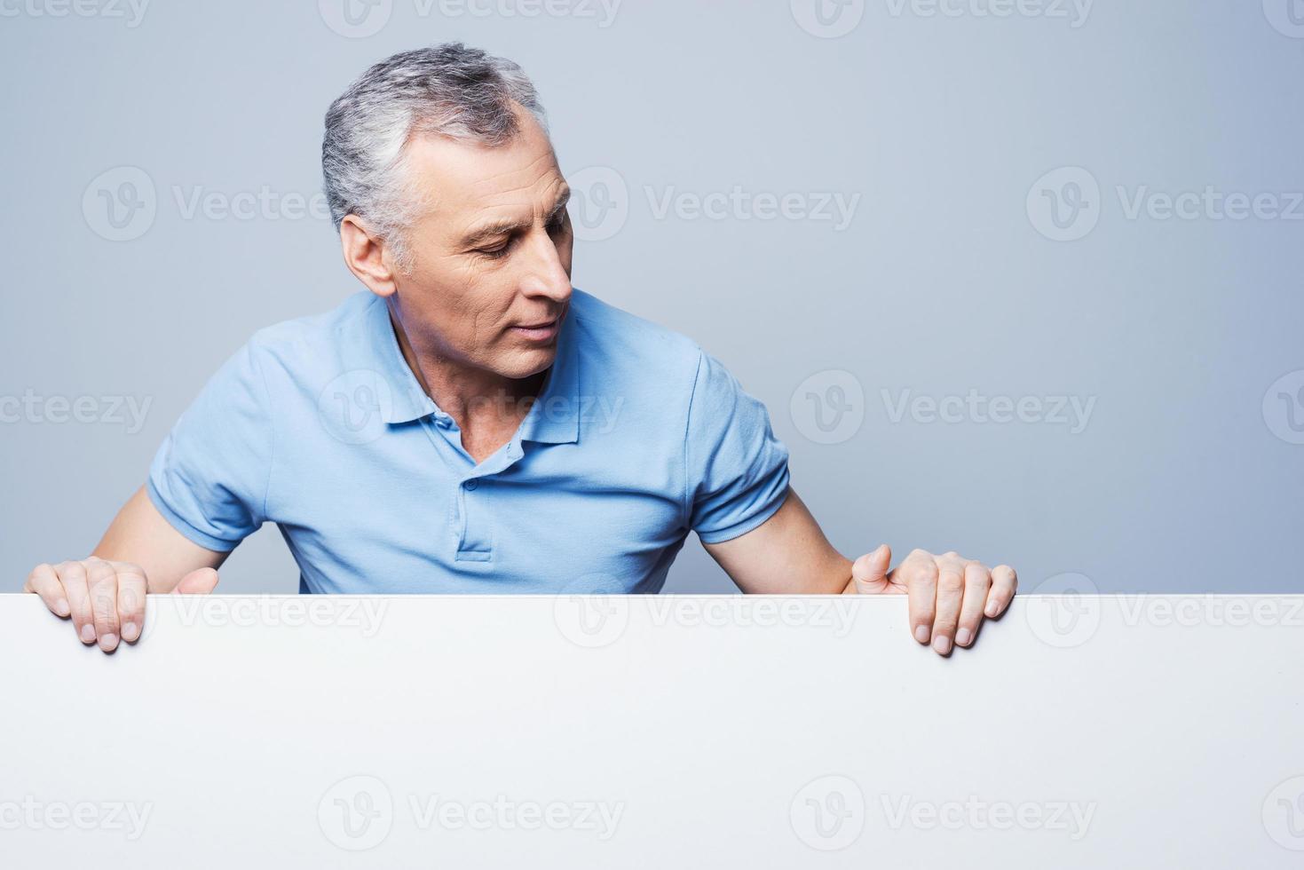 What is there Handsome senior man looking on copy space while standing against grey background photo