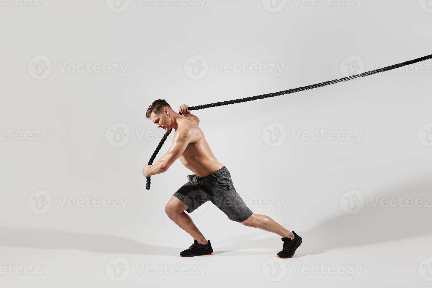 Confident young man with perfect body pulling a rope against white