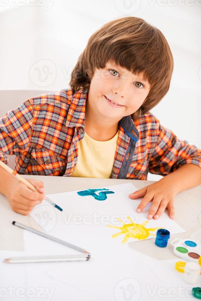 Painting. Top view of little boy relaxing while painting with watercolors sitting at the table photo