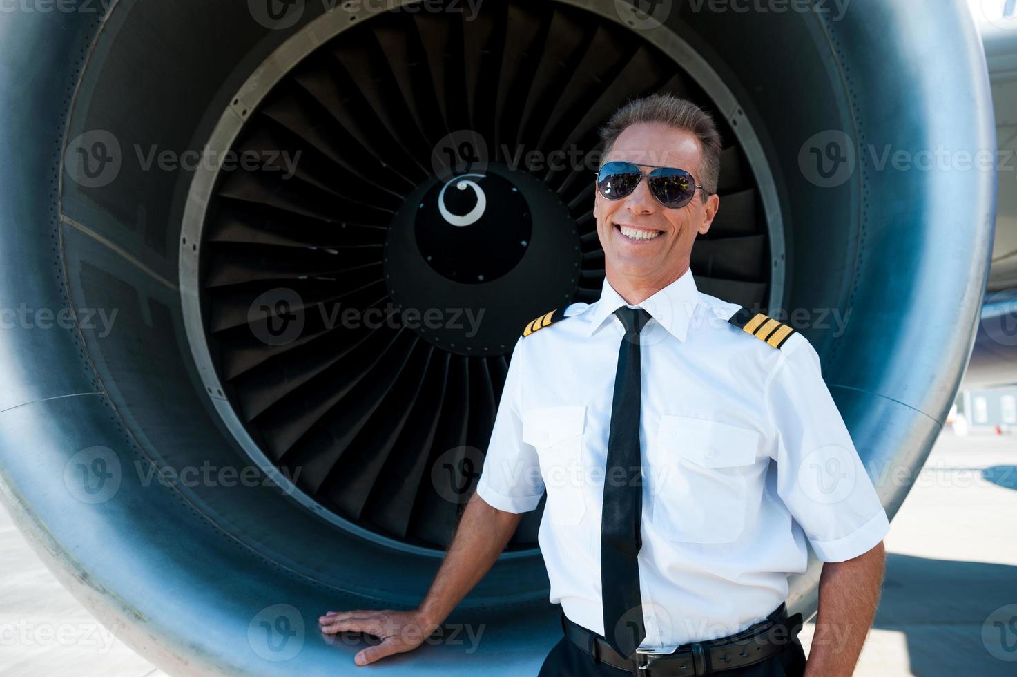 Confident pilot. Confident male pilot in uniform leaning at the turbine engine of airplane and smiling photo