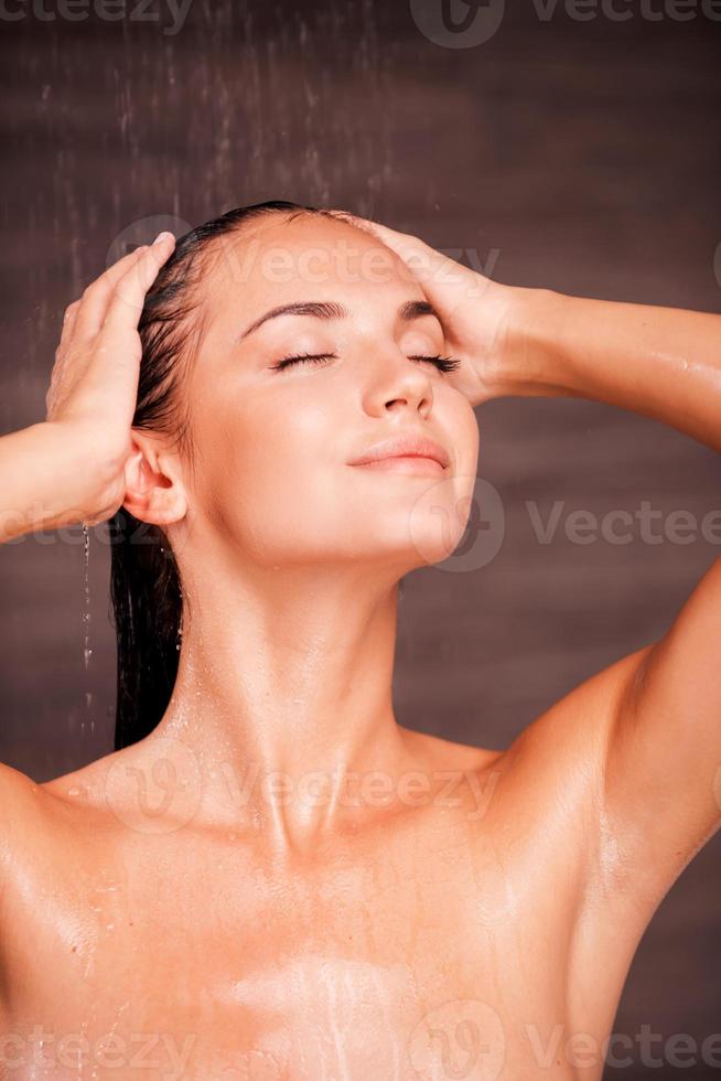 nada como una ducha caliente. hermosa joven sin camisa parada en la ducha y lavándose el cabello foto