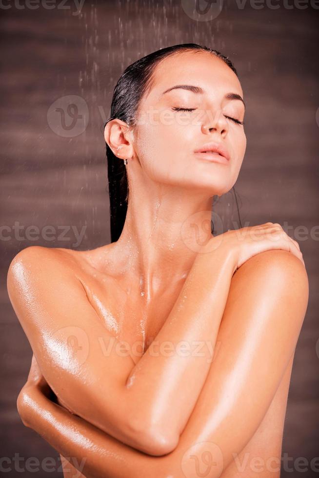 quitando el estrés. hermosa joven sin camisa parada en la ducha y lavándose el cabello foto