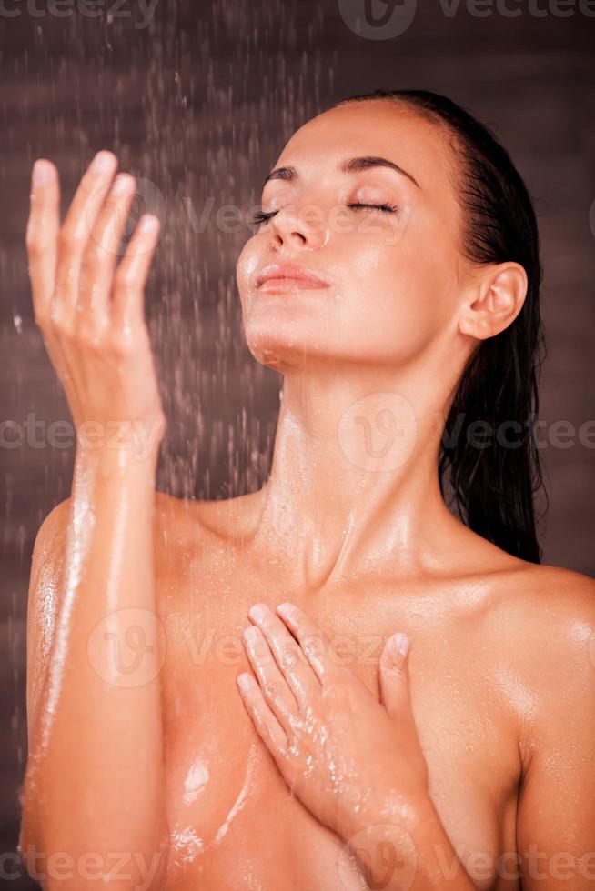 frio y fresco. hermosa joven sin camisa parada en la ducha y cubriendo los senos con las manos foto