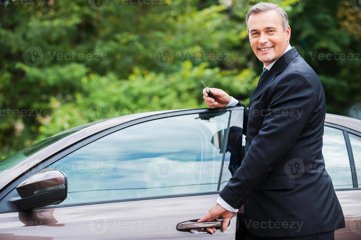 This car is perfect for me. Cheerful mature man in formalwear looking at camera and smiling while standing near his new car photo