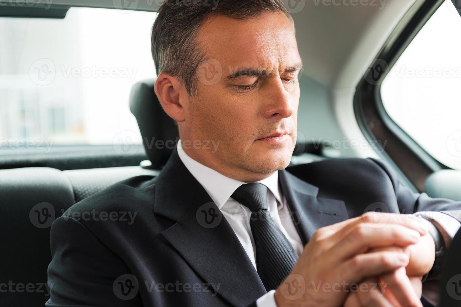 I will be in time. Confident mature businessman looking at his watch while sitting on the back seat of a car photo