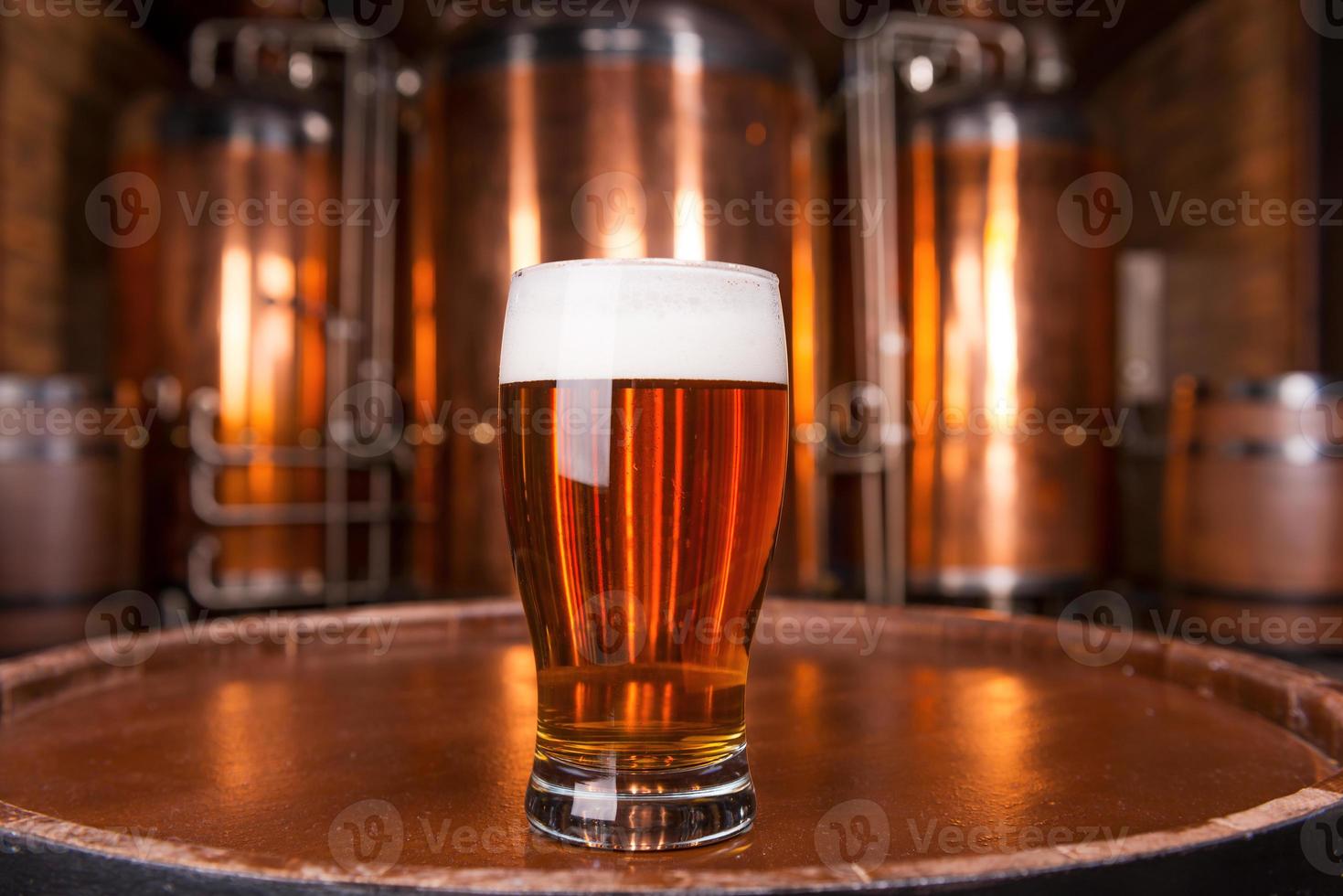 la mejor cerveza de la ciudad. primer plano de vidrio con cerveza fresca de pie en el barril de madera con recipiente de metal en el fondo foto