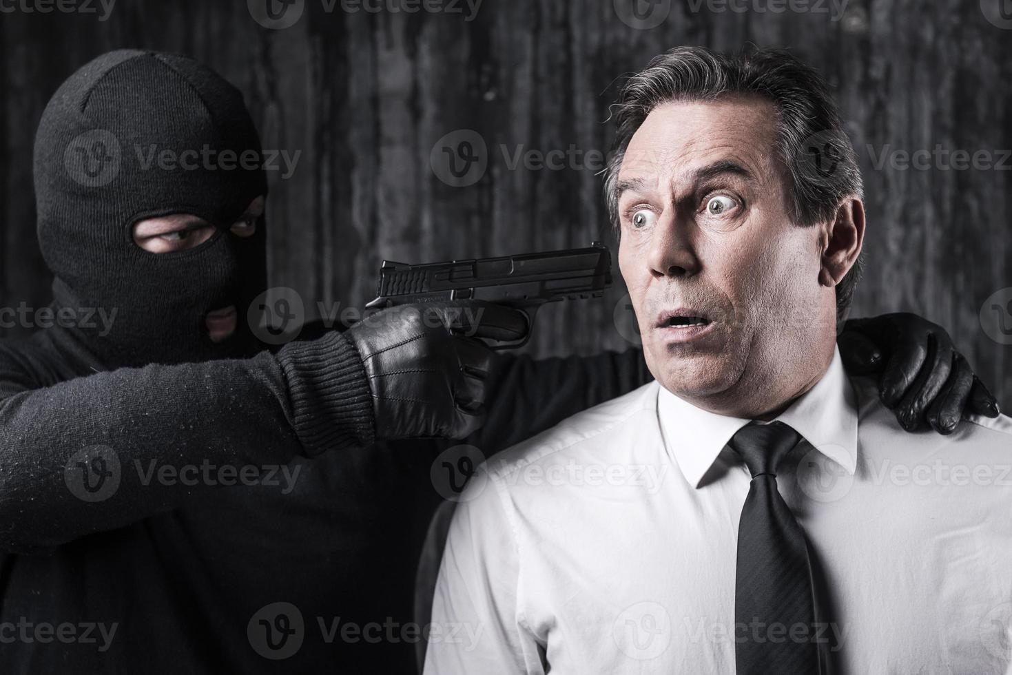 Victim of violence. Shocked businessman caught by a criminal aiming his head with gun photo