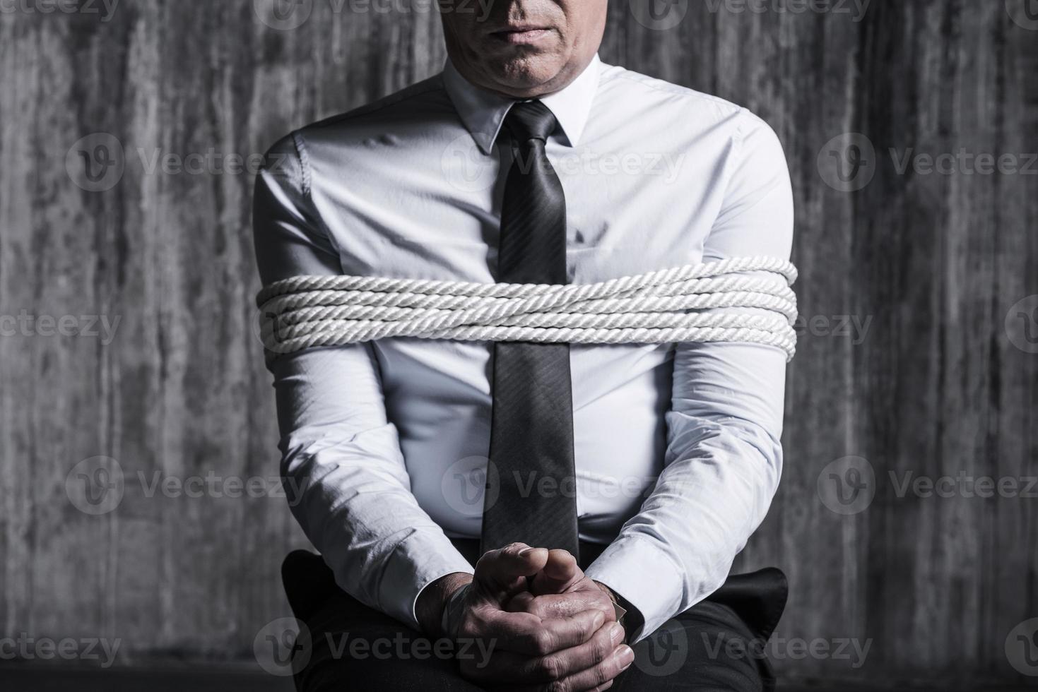 Fear and hopelessness. Cropped image of tied up businessman sitting at the chair with dirty wall  in the background photo