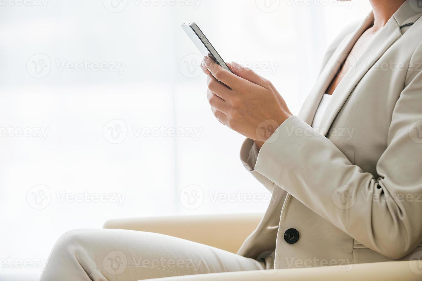 Typing business message. Side view of businesswoman in suit typing something on mobile phone while sitting at the chair photo