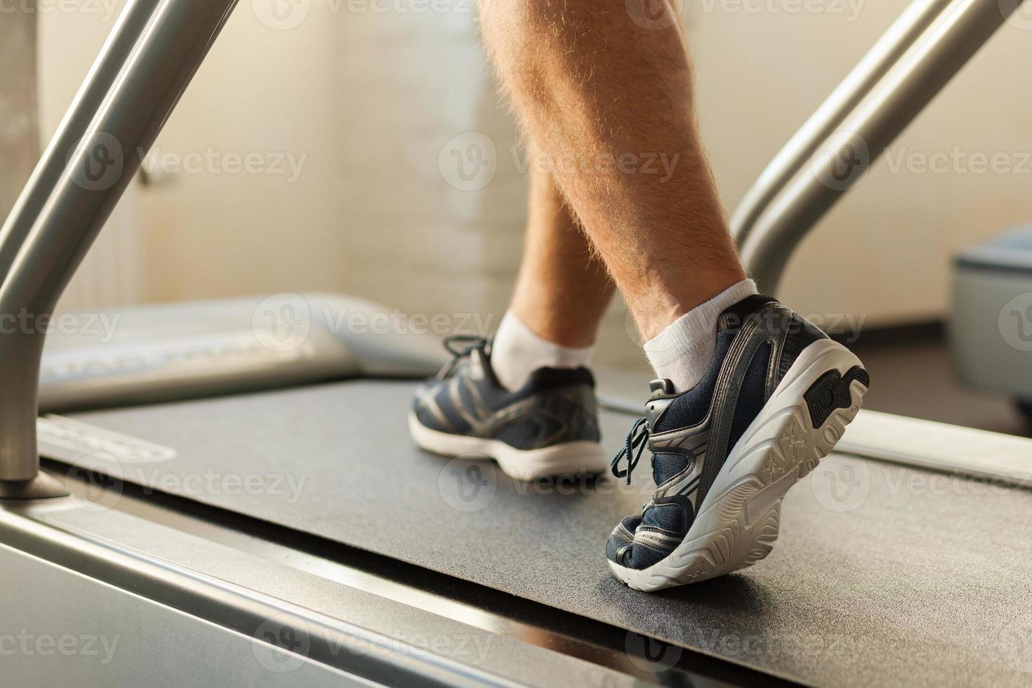 Exercising on treadmill. Close-up of man walking by treadmill in sports club photo