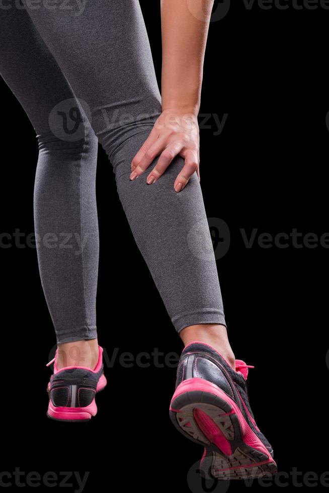 Pain in shin. Close-up of woman touching her shin while standing against black background photo