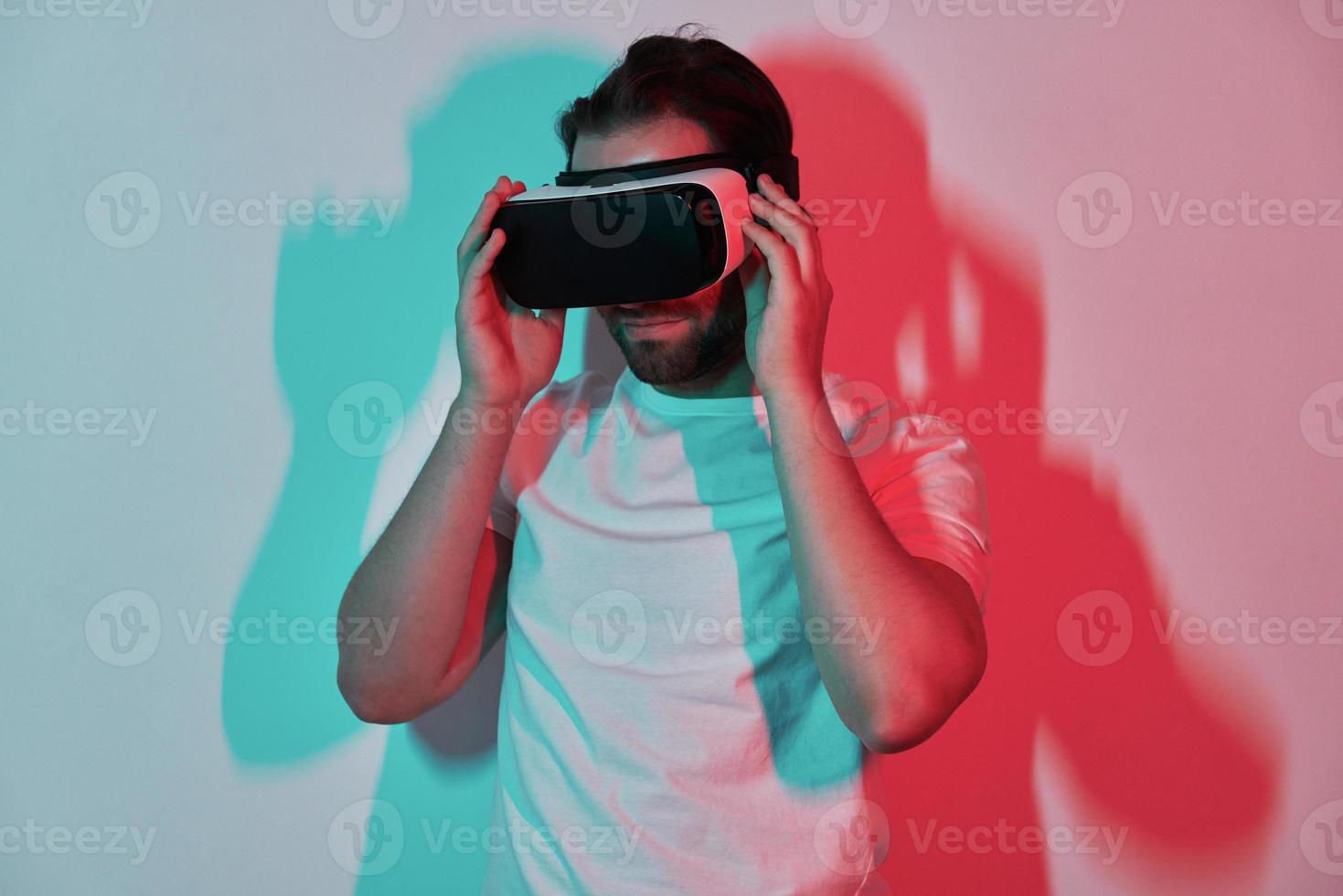 Confident young man adjusting his virtual reality eyeglasses with colorful shadows in the background photo