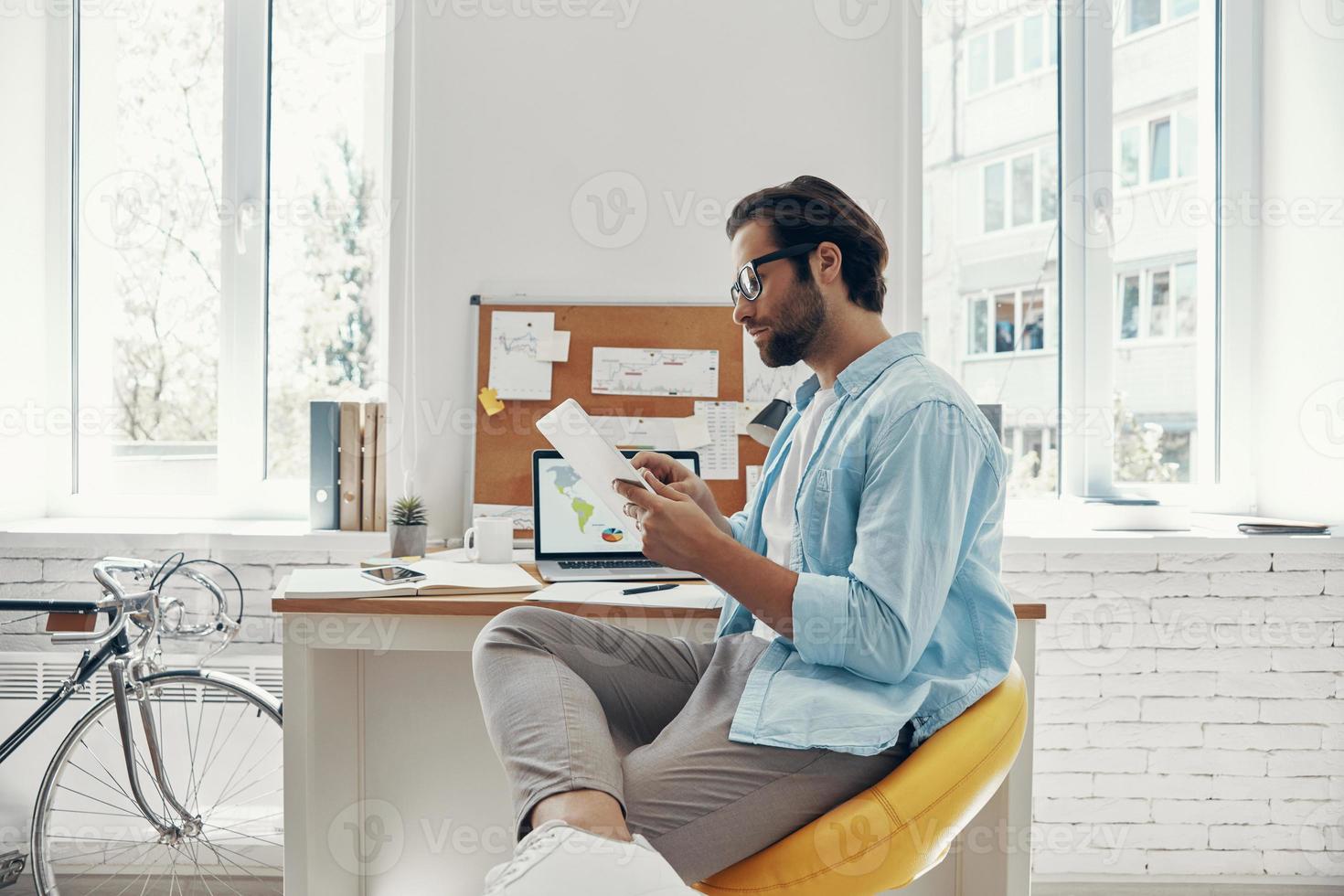 Confident young man using digital tablet while sitting at his working place photo