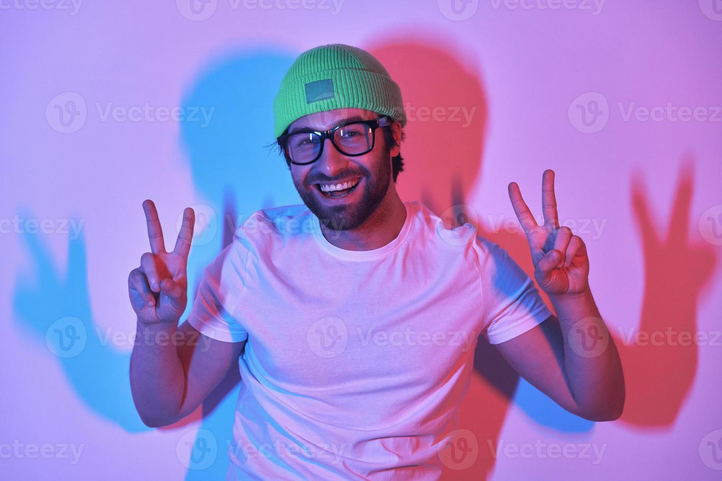 Handsome young man in funky hat gesturing and smiling while standing against colorful background photo