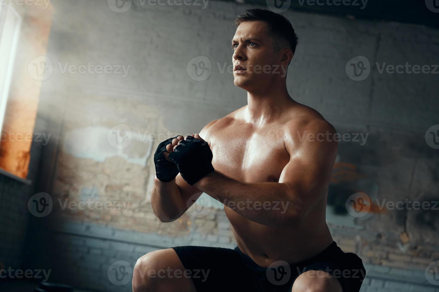 Confident young man standing in squatting position while training in gym photo