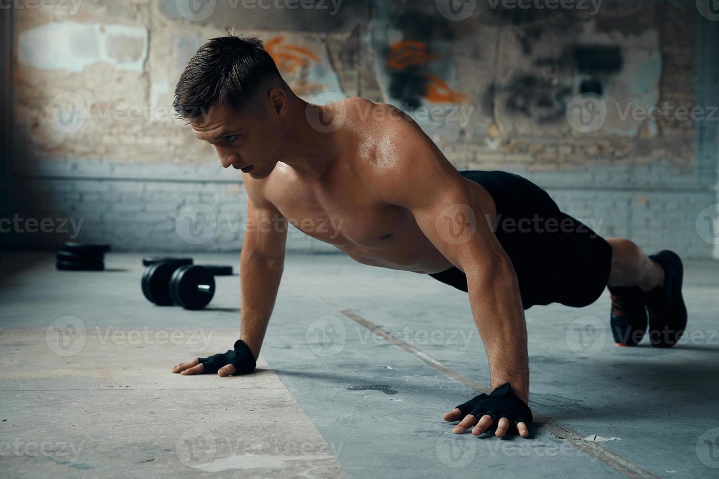 Confident young man doing push-up exercises in gym photo