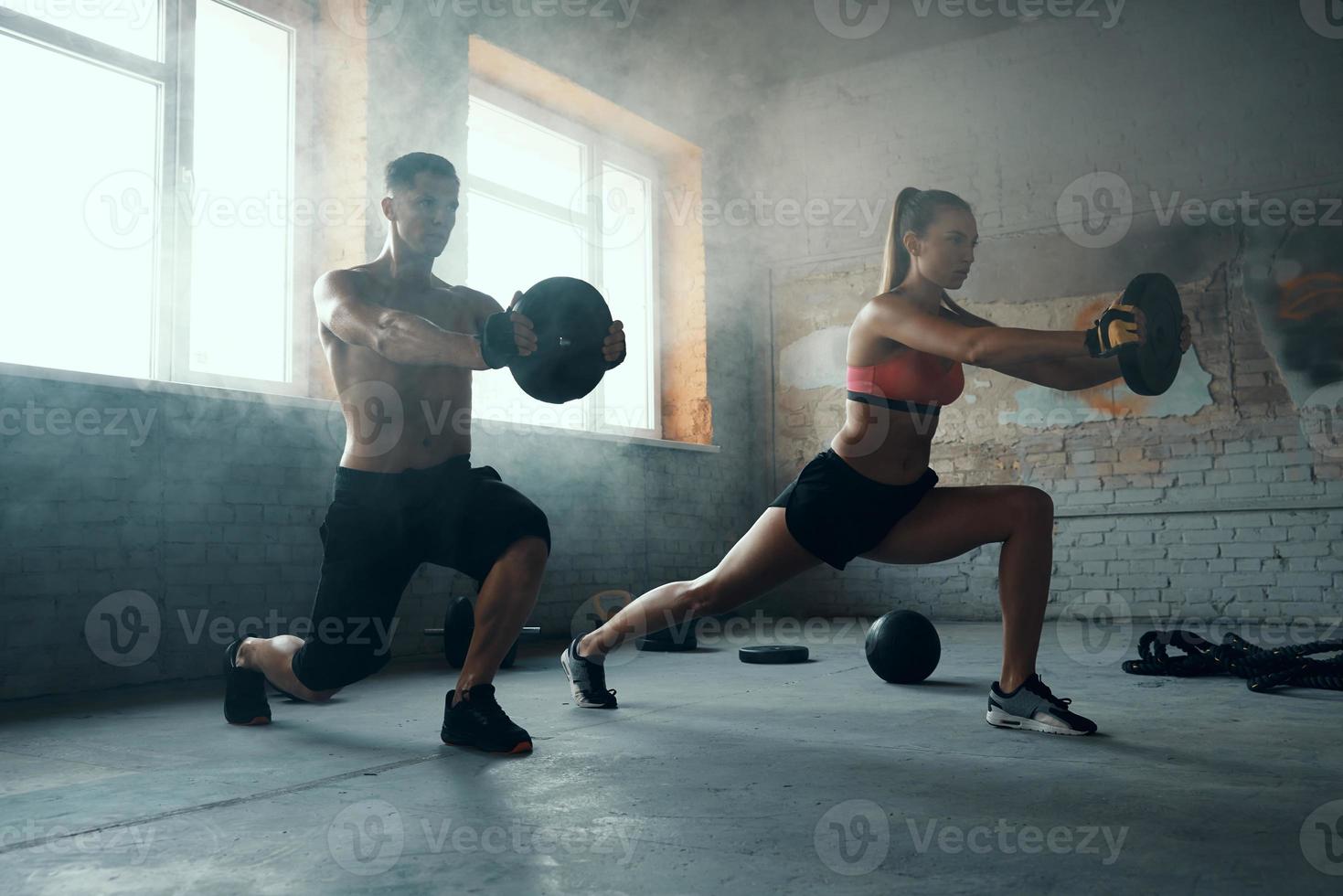 pareja joven en forma que parece concentrada mientras hace entrenamiento con pesas en el gimnasio foto