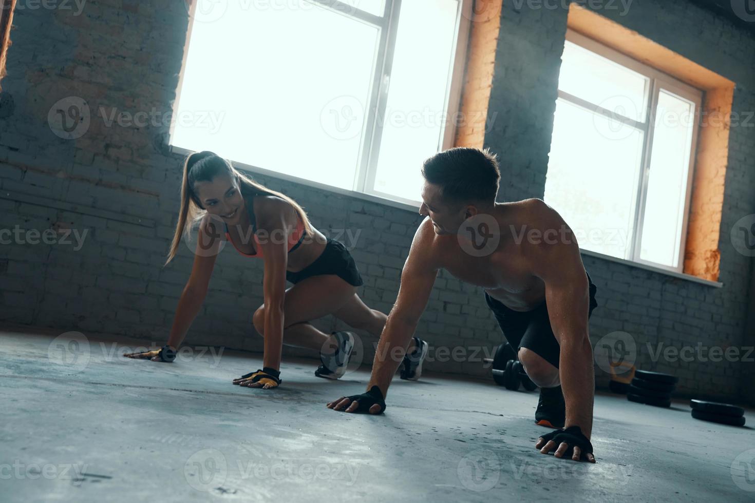 pareja joven en forma mirándose y sonriendo mientras hacen ejercicio juntos en el gimnasio foto