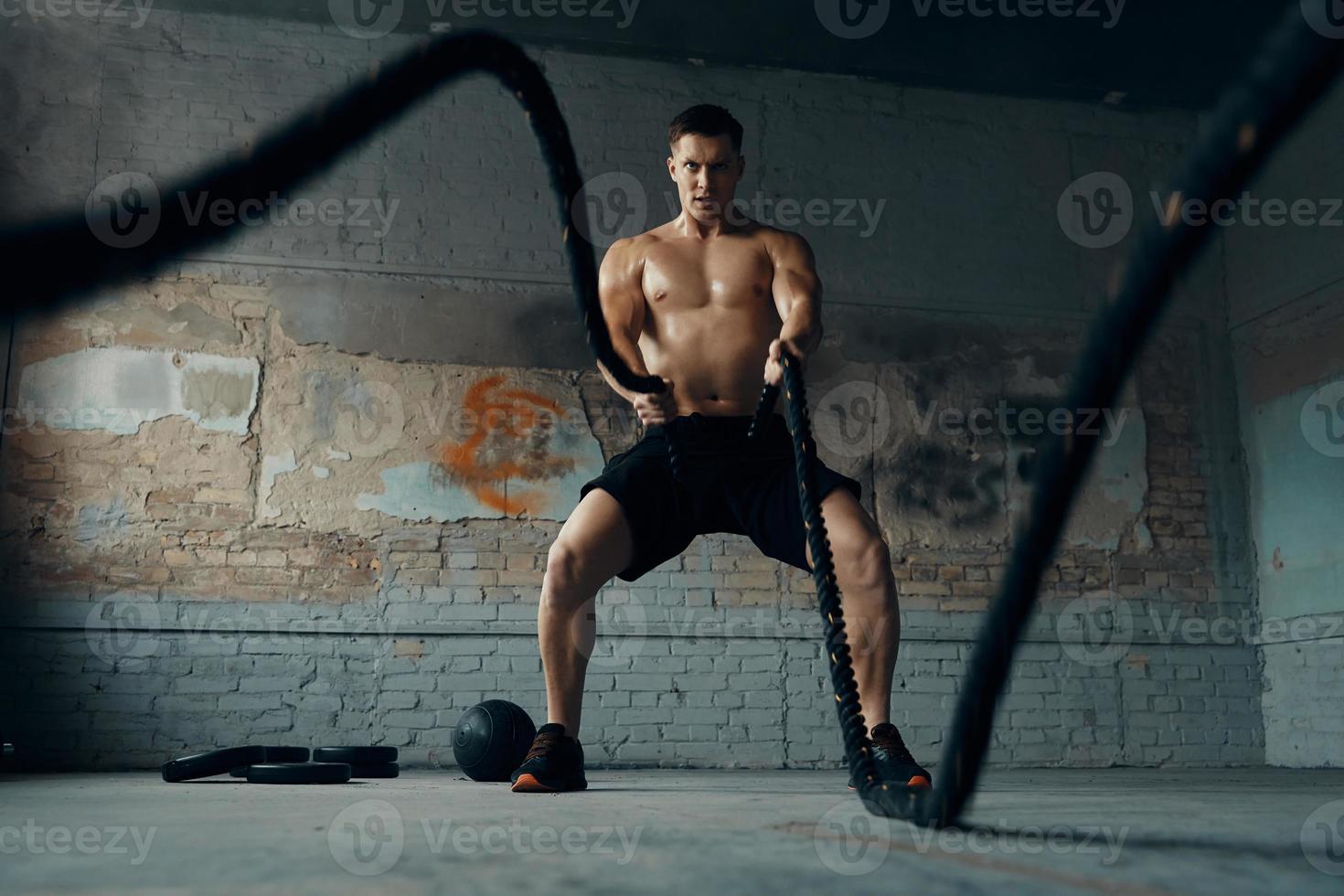 joven confiado haciendo ejercicio con cuerda de batalla en el gimnasio foto