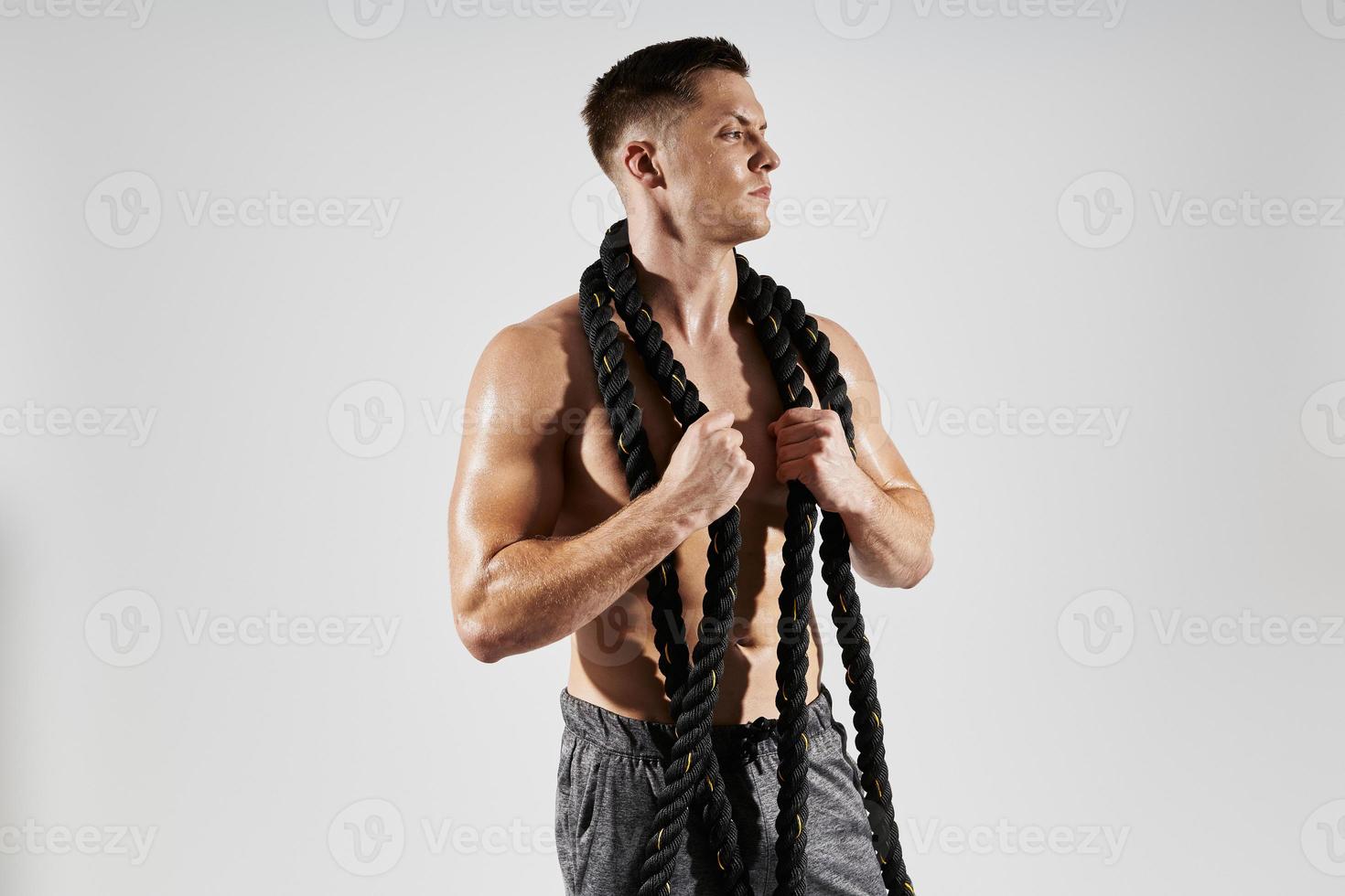 Handsome young man with perfect torso carrying rope on shoulders against white background photo