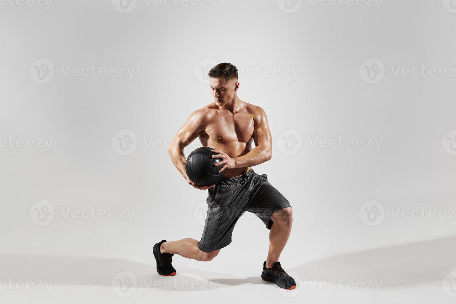 Concentrated young man with perfect body exercising with medicine ball against white background photo
