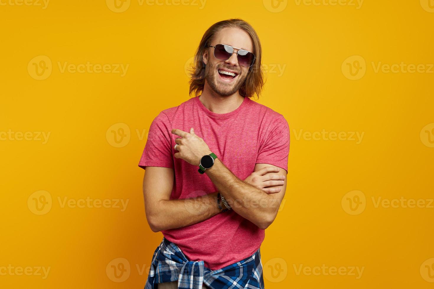 Handsome young man pointing away and smiling while standing against yellow background photo