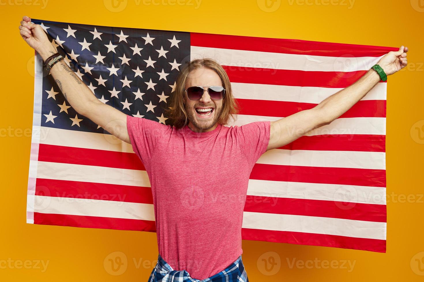 Happy young man carrying American flag while standing against yellow background photo