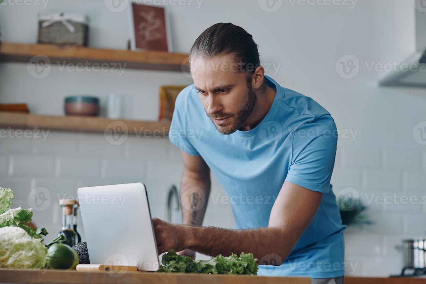 Handsome young man using digital tablet while preparing food at the domestic kitchen photo
