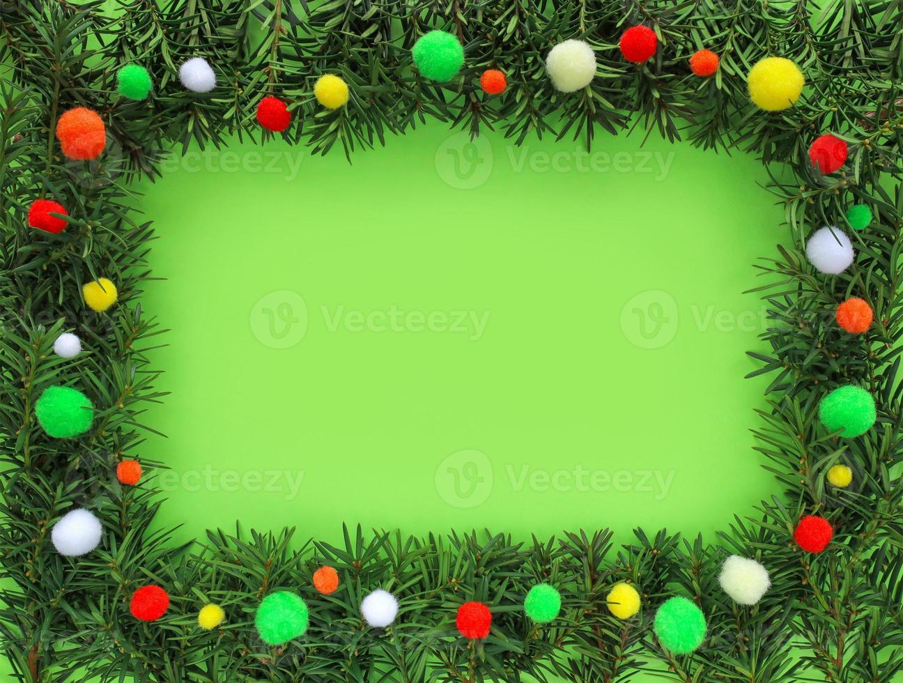 Christmas green frame made of fir tree branches around on light green background, space for text in the center. Border decorated colorful pom poms. Happy holiday Xmas and New Year concept. photo