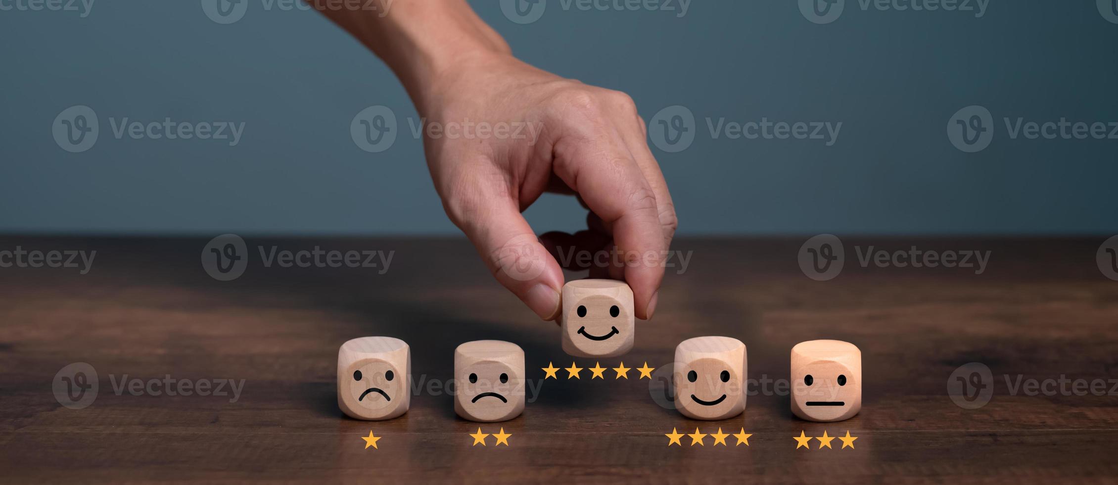 Man hand pick up wooden smiling face box with five star rating icon for feedback review satisfaction service, Customer service experience and business satisfaction survey. photo