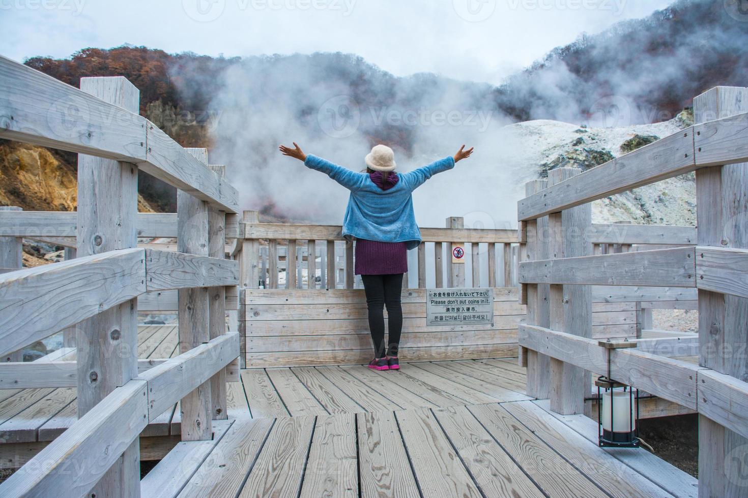 mujer de pie en jigokudani o valle del infierno en la ciudad de noboribetsu onsen, respiraderos de vapor caliente, arroyos sulfurosos y otra actividad volcánica, aguas termales, hokkaido, japón, concepto de viaje. foto