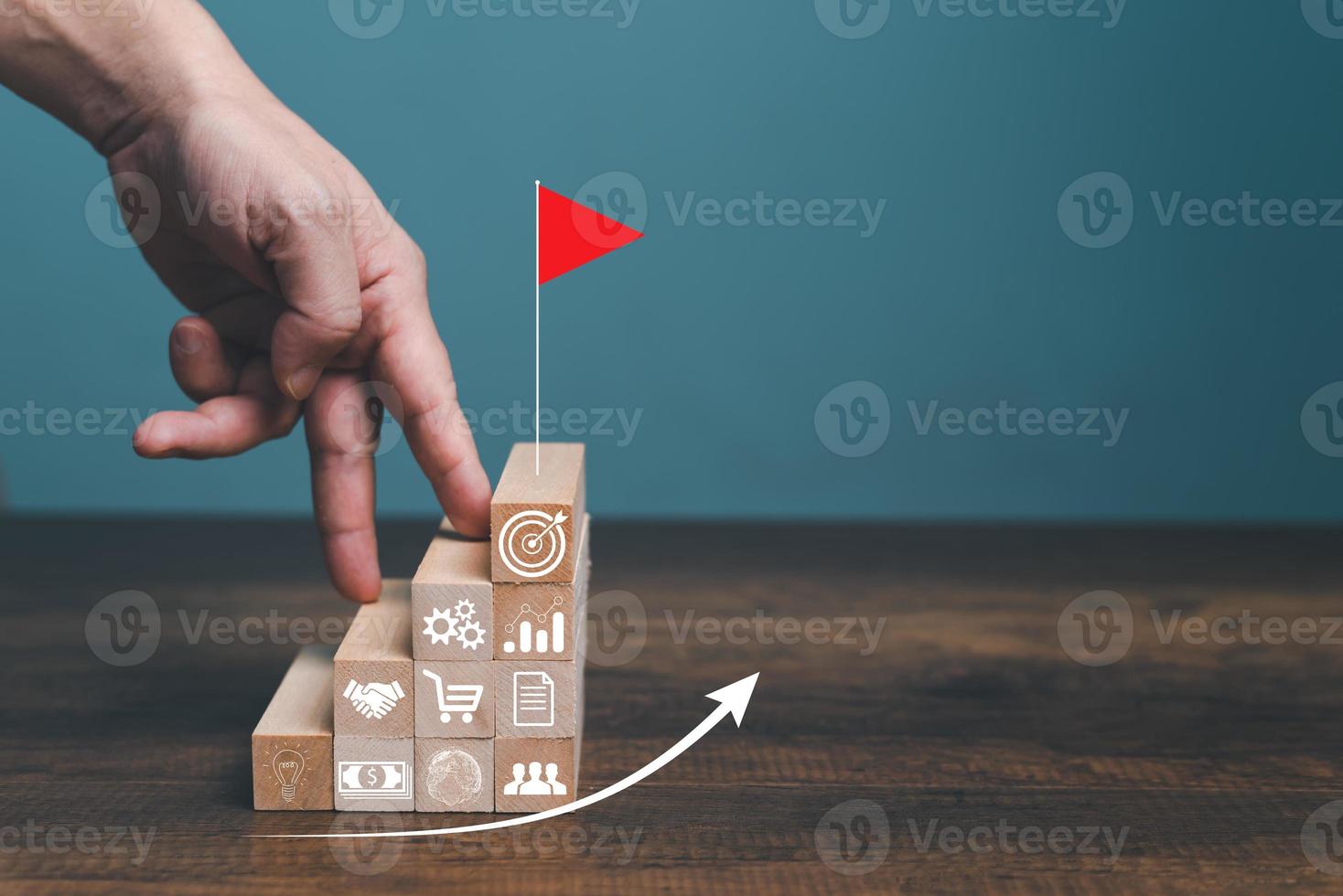 Step by step to grow your business, business success or career path success concept. Man use finger walking up to the top target with red flag on wooden blocks arranged in a shape of staircase. photo