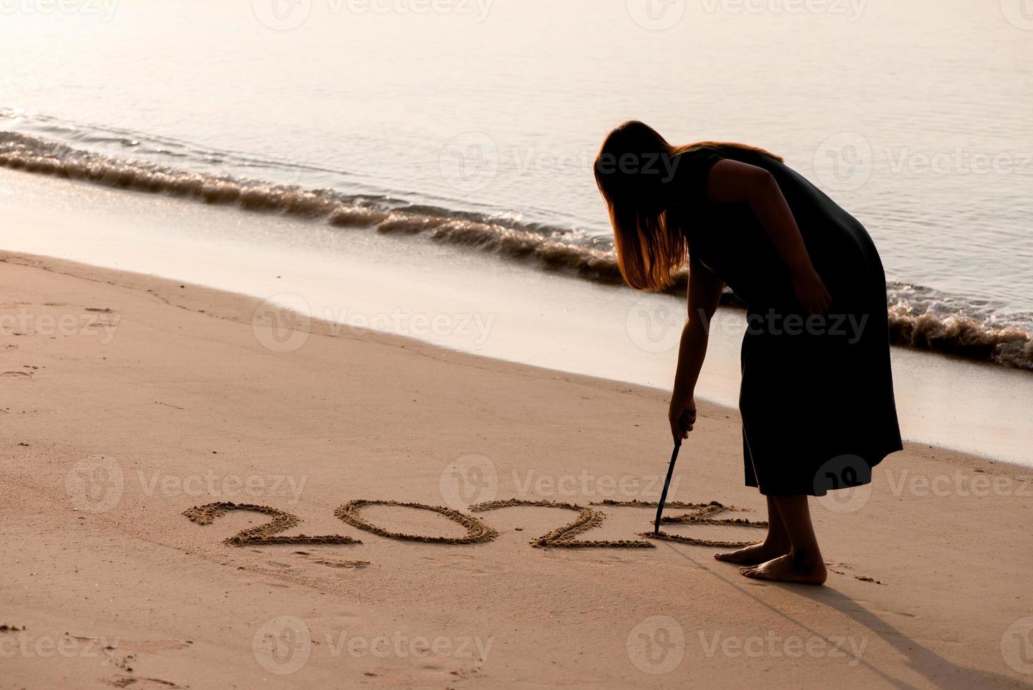2023 Happy New Year, Young healthy woman writing 2023 number on the sand beach at sunrise, health care, health insurance, healthy life concept. photo