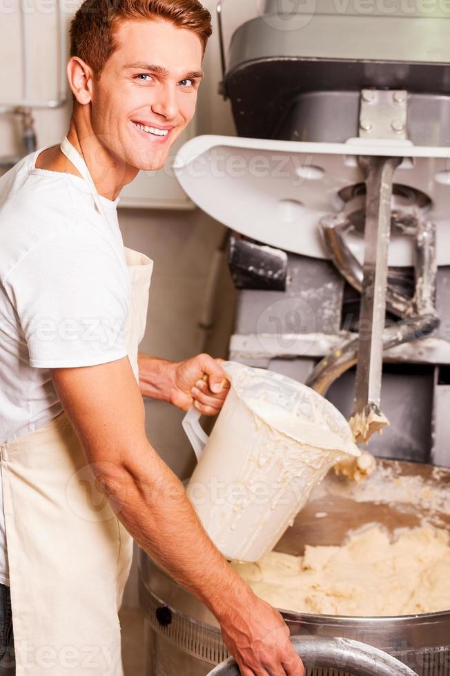 The best dough for our pastry. Confident young man in apron pushing button on dough mixing machine and smiling photo