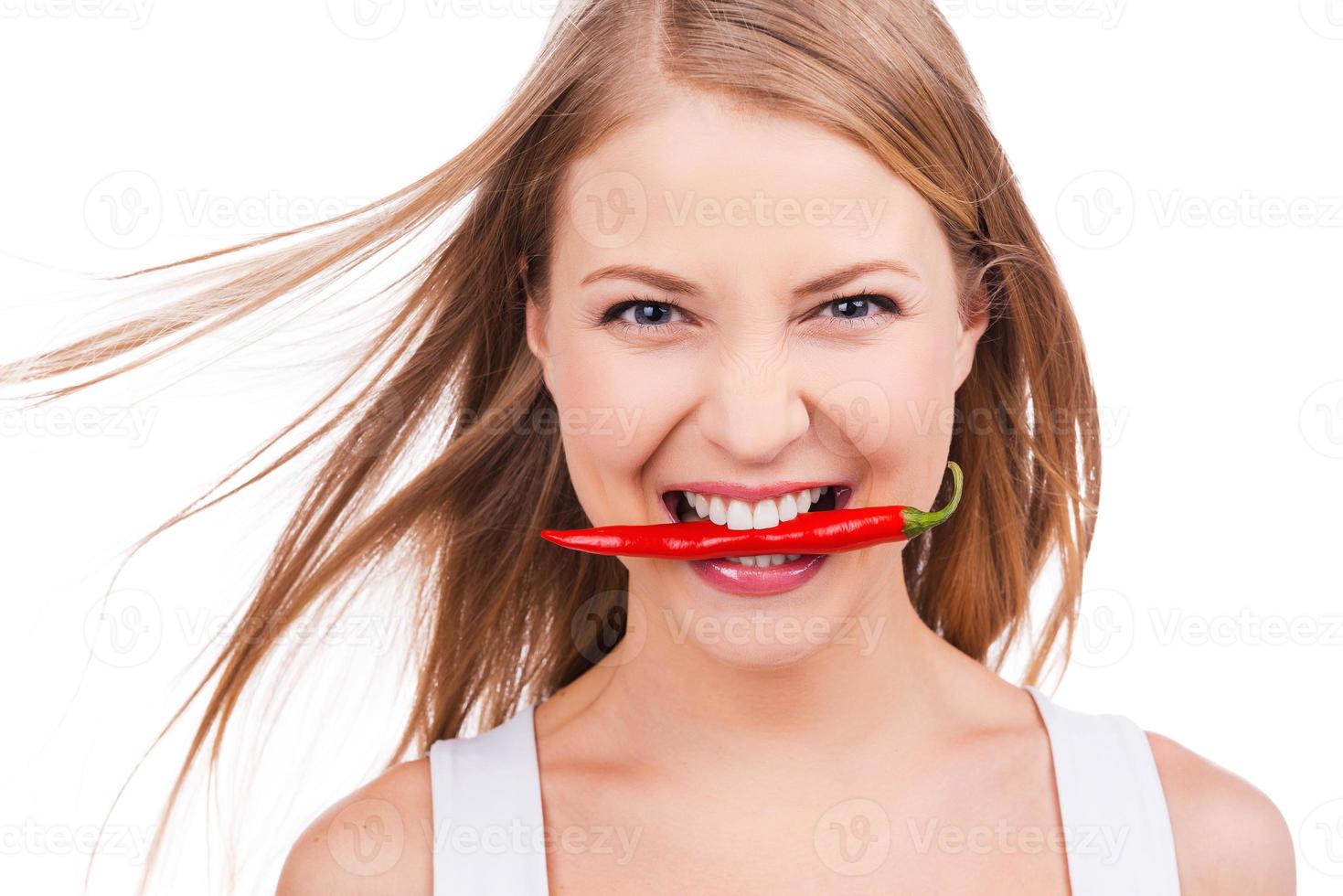 descarada como esta pimienta hermosa mujer joven sosteniendo ají en los dientes mientras está de pie contra el fondo blanco foto