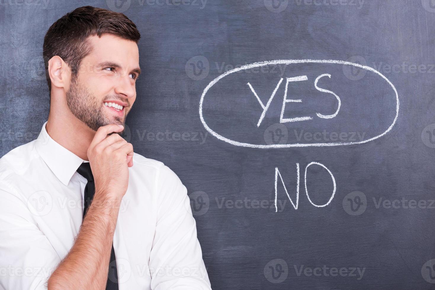 The best answer. Handsome young man holding hand on chin and looking on chalk drawing on blackboard photo