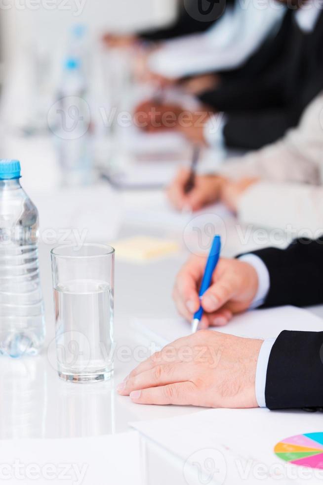 Business people at work. Close-up of business people writing something in their note pads while sitting in a row photo