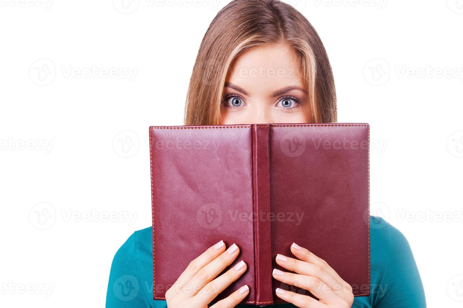 I want to know everything. Terrified young woman looking out of the book while standing against white background photo