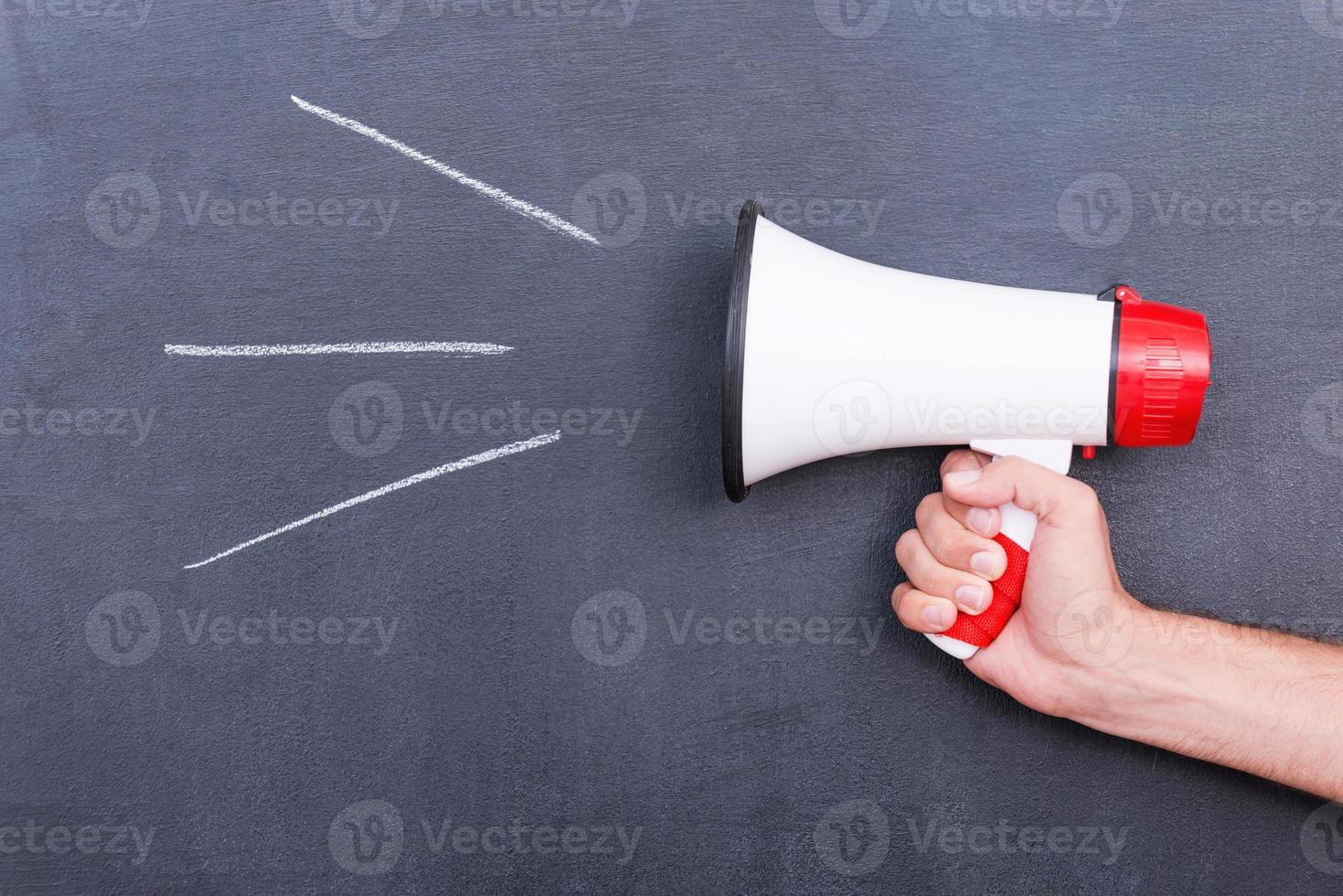 Megaphone . Close-up of human hand holding megaphone against blackboard photo