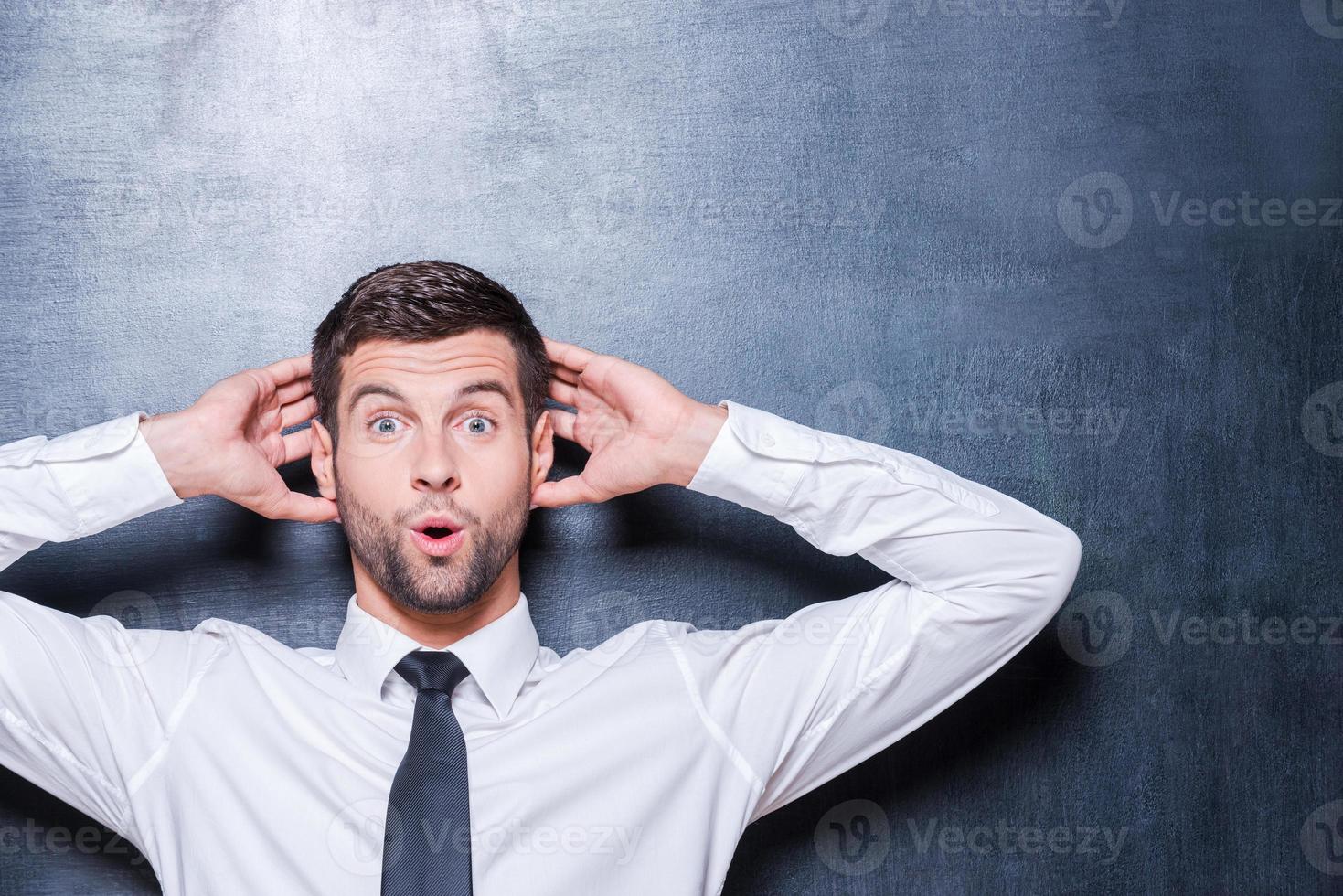 Shocking news. Surprised young man in shirt and tie expressing positivity and gesturing while standing against blackboard photo