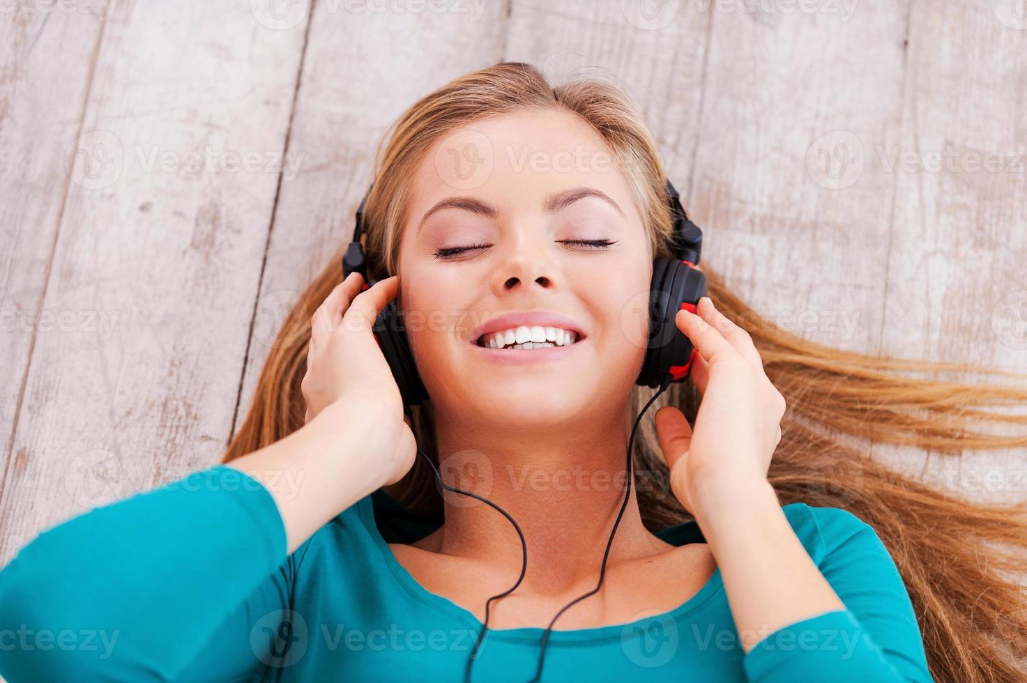 profundamente en la música. vista superior de una hermosa joven tendida en el suelo en su apartamento escuchando música a través de auriculares foto