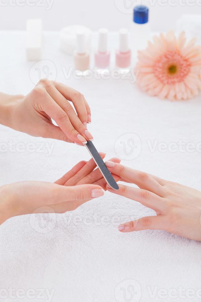 Preparing nails for manicure. Close-up of beautician polishing nails of female customer photo