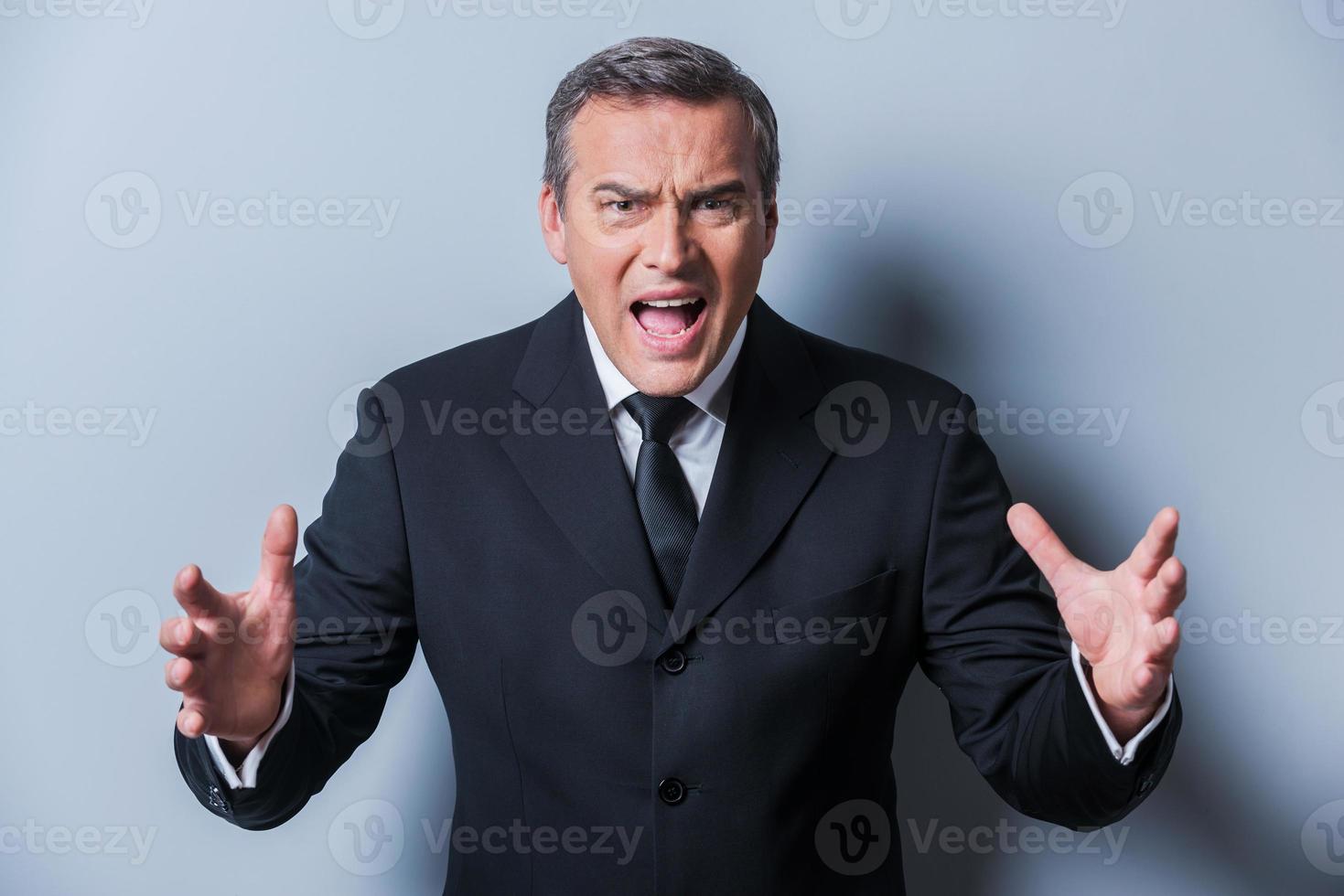Furious boss. Furious mature man in formalwear gesturing and looking at camera while standing against grey background photo