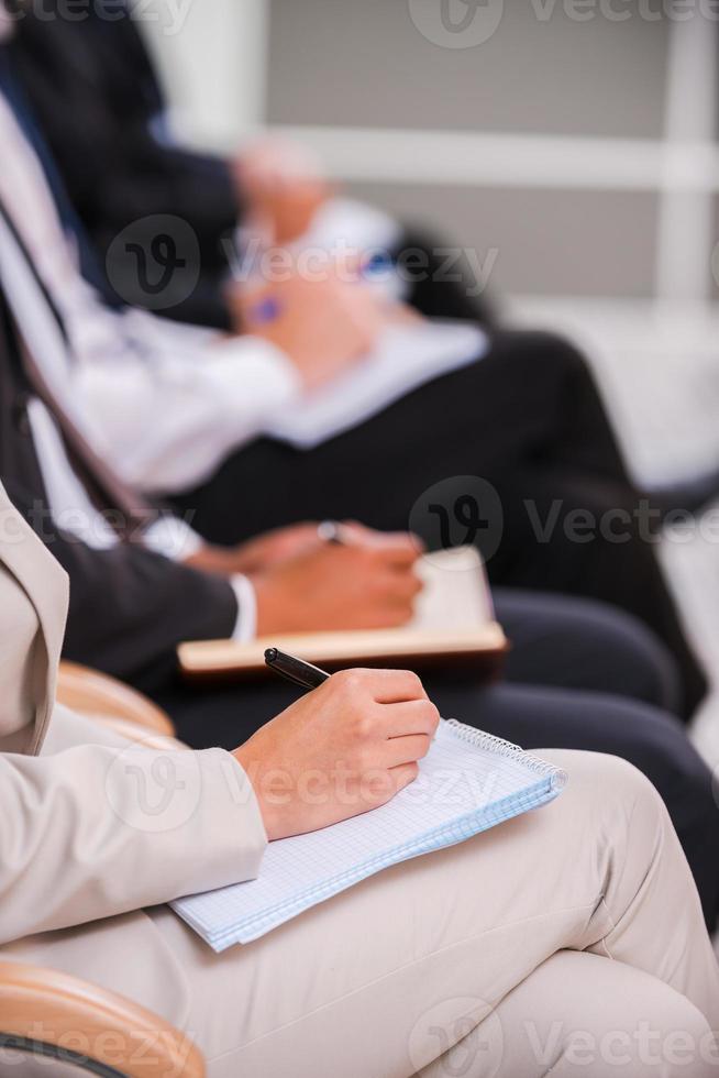 People making notes. Close-up side view of business people writing something in their note pads while sitting in a row photo