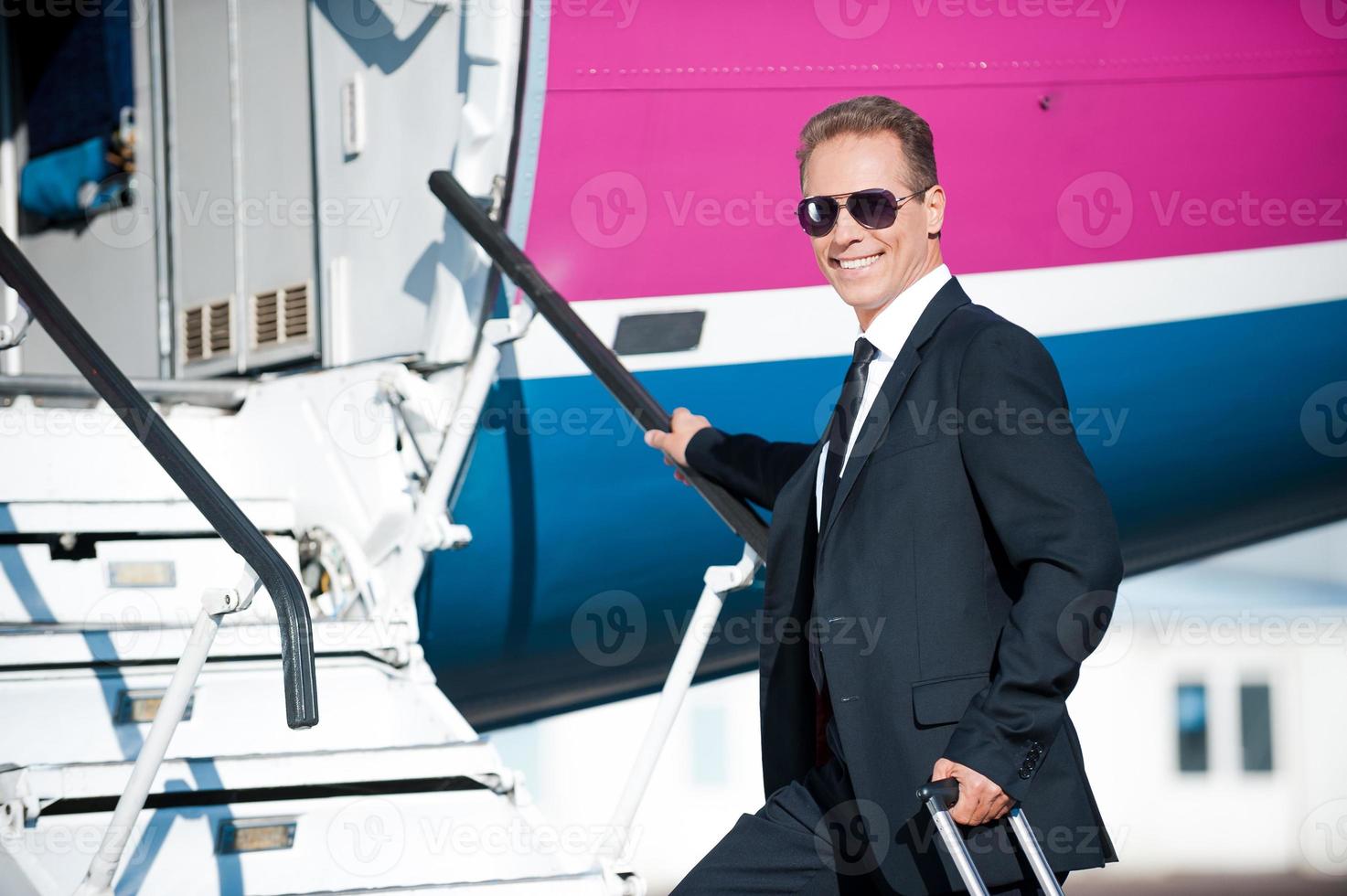Business calling. Confident mature businessman moving up by airplane ladder to the entrance photo
