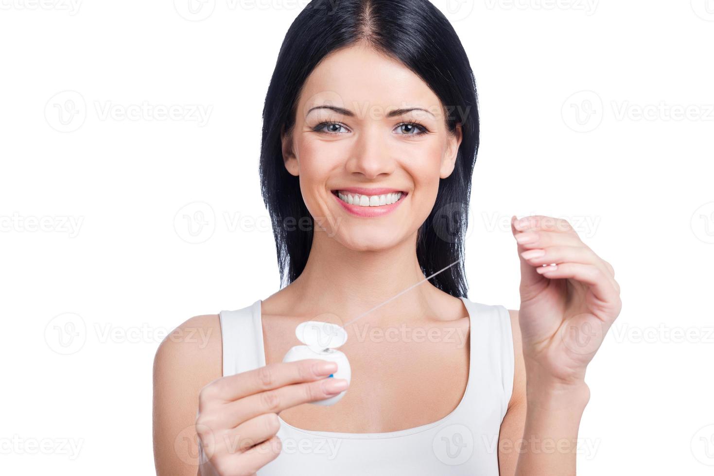 Dental cleaning. Beautiful young woman holding dental floss and smiling at camera while standing against white background photo