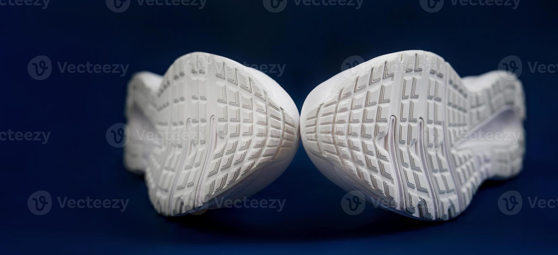 The white sole of sneakers on a dark blue background. A couple of white sneakers. photo