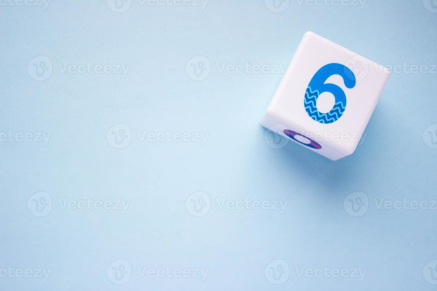 Close-up photo of a white plastic cube with a blue number 6 on a blue background in the upper right corner. With copy space