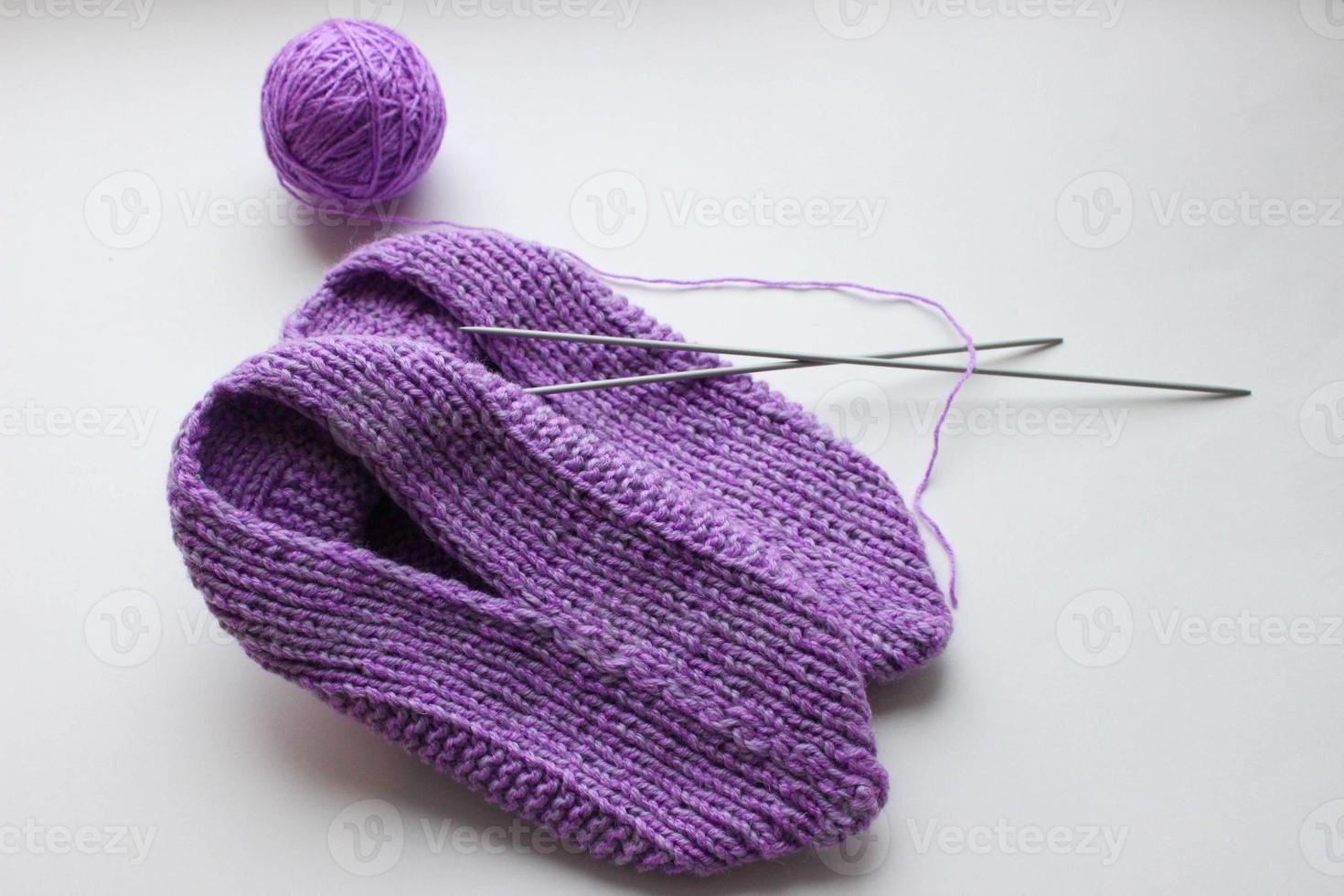 Handmade knitted pink slippers with knitting needles and ball of yarn on white background photo