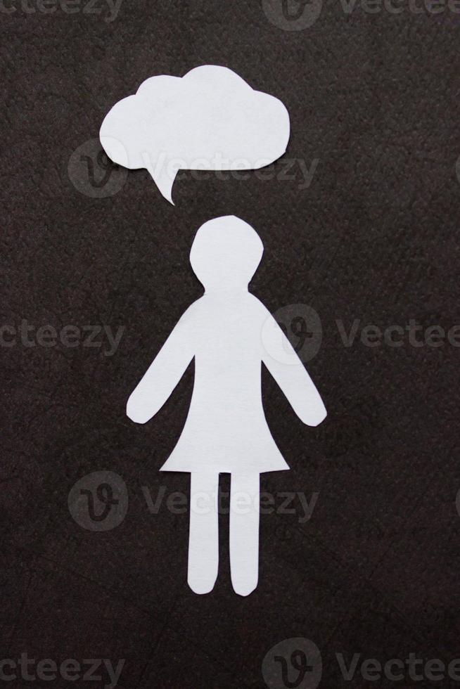 The silhouette of a woman in a dress made of white paper, cut by hand. With speech-bubble in the center of the photo on black background